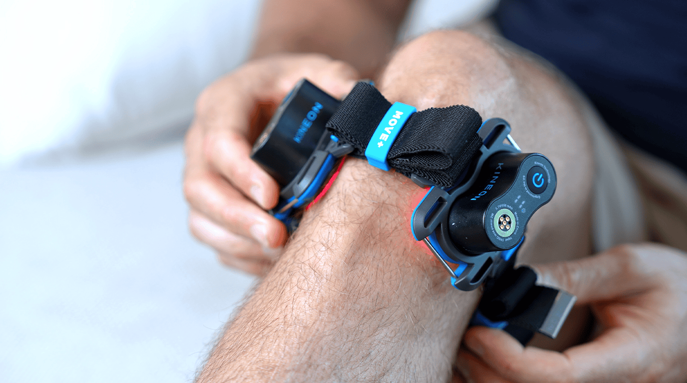 Close-up of the Kineon MOVE+ red light therapy device strapped around a knee with the 808nm laser glow active